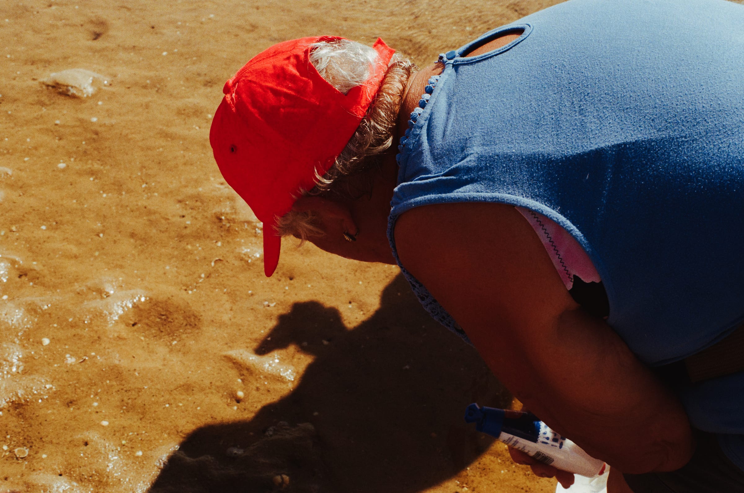 Une femme à casquette rouge penchée sur le sable, un flacon à la main, guette les trous des couteaux.